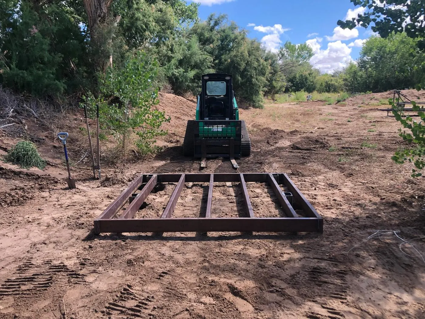 Welded steel deck frame on cleared ground with a track loader behind it